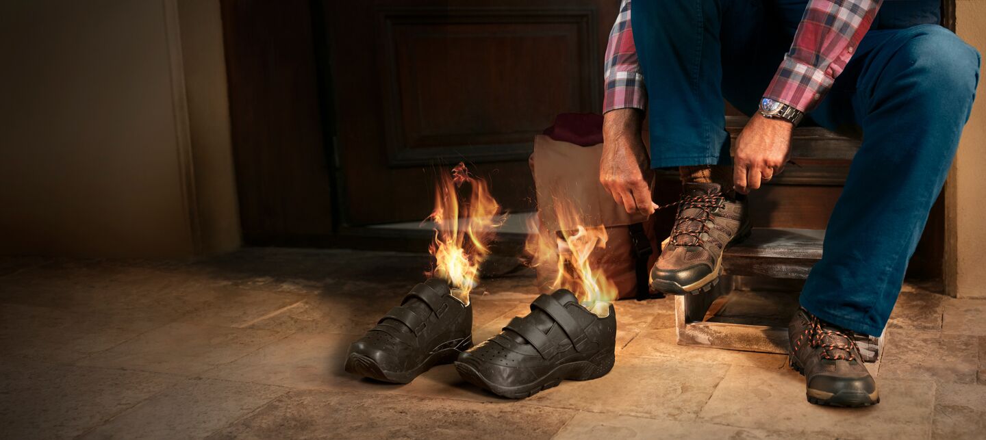 Illustration of a person on front steps of their house putting shoes on in preparation for a hike as the inside of shoes next to him are on fire